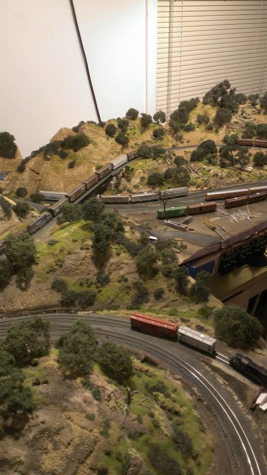 MY N SCALE MODEL RAILROAD AN OVERVIEW OF MY LAST LAYOUT DEPICTING THE FOOTHILLS OF CALIFORNIA. TRAINS ARE CROSSING OVER AND UNDER A BRIDGE AND VARIOUS OAK TREE SPECIES DOT THE GOLDEN LANDSCAPE.