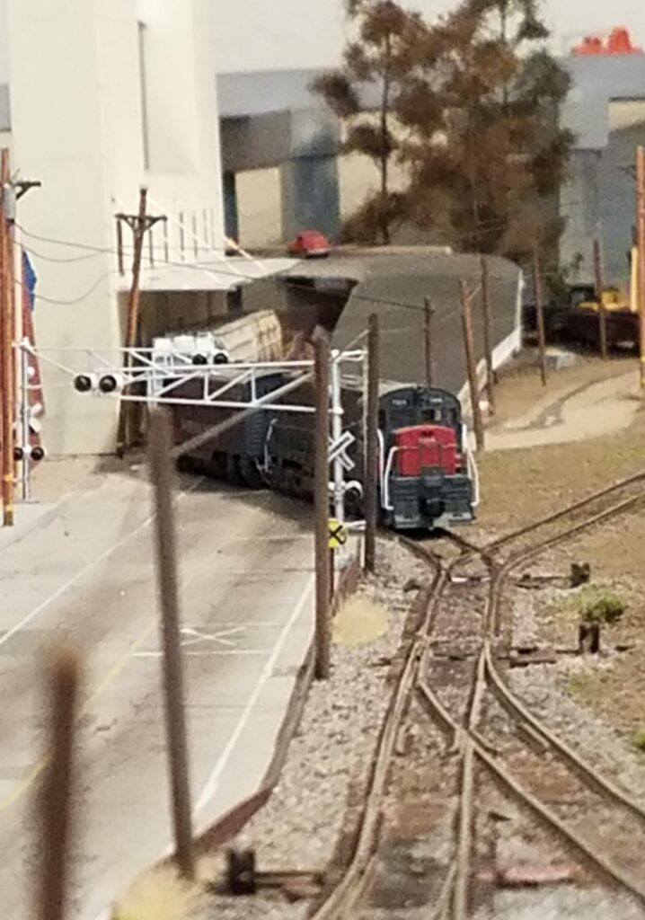 AN N-SCALE U30C LOCOMOTIVE ON MY LAYOUT IN THIS PHOTO, SHOT IN A GRAINY VINTAGE STYLE TECHNIQUE, A GE U30C LOCOMOTIVE IS PULLING SOME FREIGHT CARS FROM THE GENERAL MILLS FACTORY ACROSS THE ROADWAY.